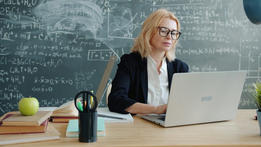 Teacher using chatgpt prompts for grammar lessons on a laptop in front of a chalkboard