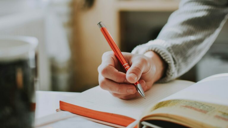 Teacher marking written English work with a red pen against rubric criteria