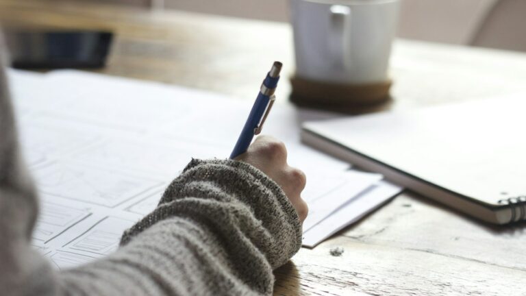 Teacher drafting an ESL lesson plan by hand in a notebook at a desk