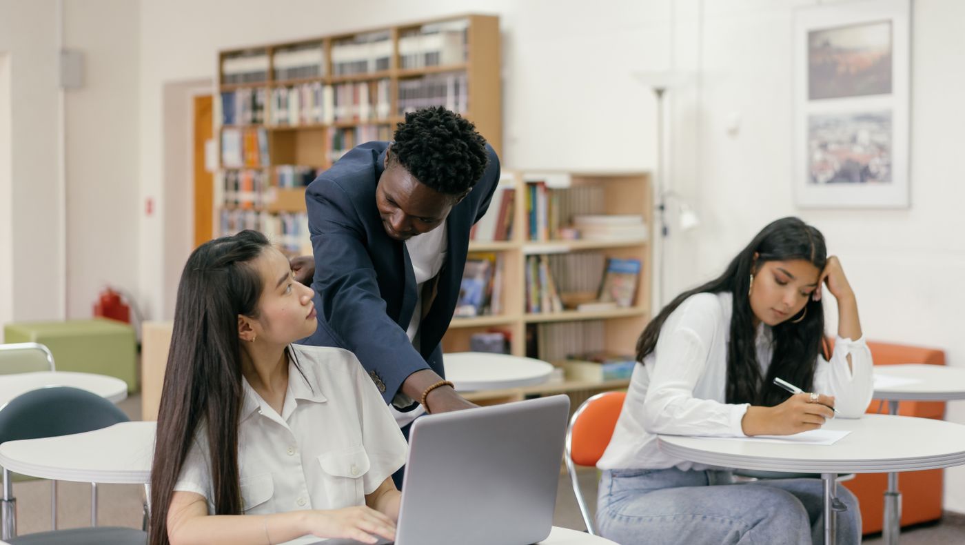 Teacher guiding a student through an AI supported English task on a classroom laptop