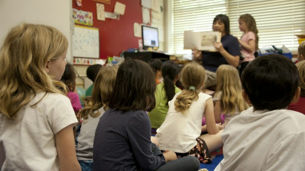 Young children sitting together listening to an English teacher read a story aloud