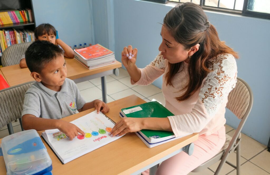 Teacher recasting a learner error while pointing at a workbook in an English language classroom